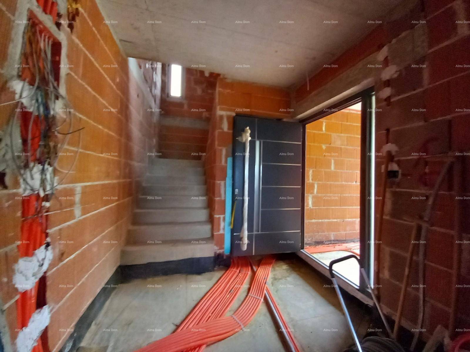 Eingangsbereich im Rohbau mit Treppe, installierter Haustür und sichtbaren Leitungen.