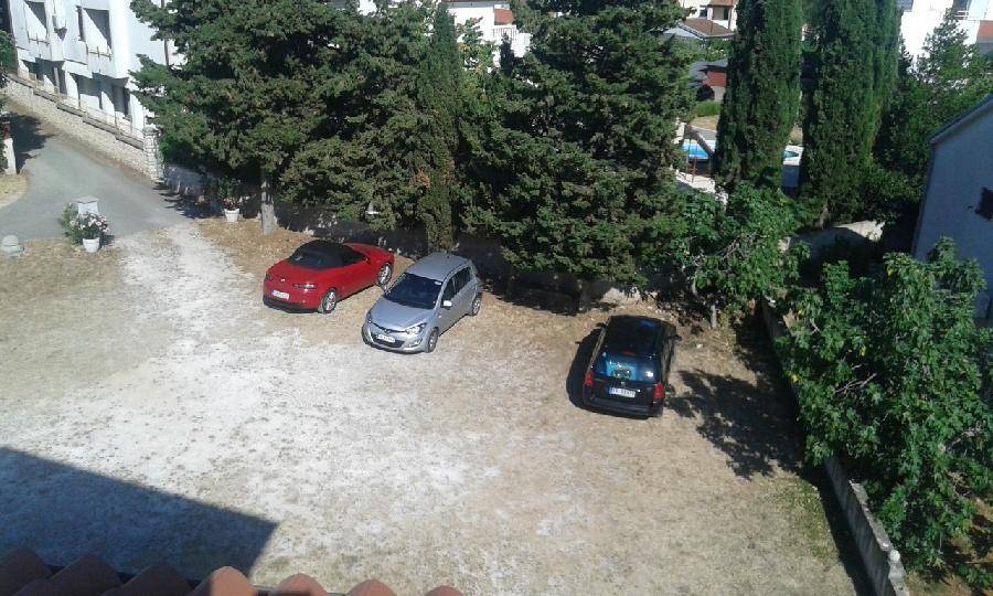 Eine erhöhte Ansicht eines Außenparkplatzes mit drei Autos, umgeben von Bäumen und einer Mauer.