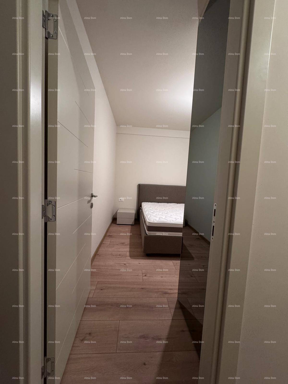 Schlichtes Schlafzimmer mit Holzboden und einem Einzelbett, durch eine Türöffnung sichtbar.