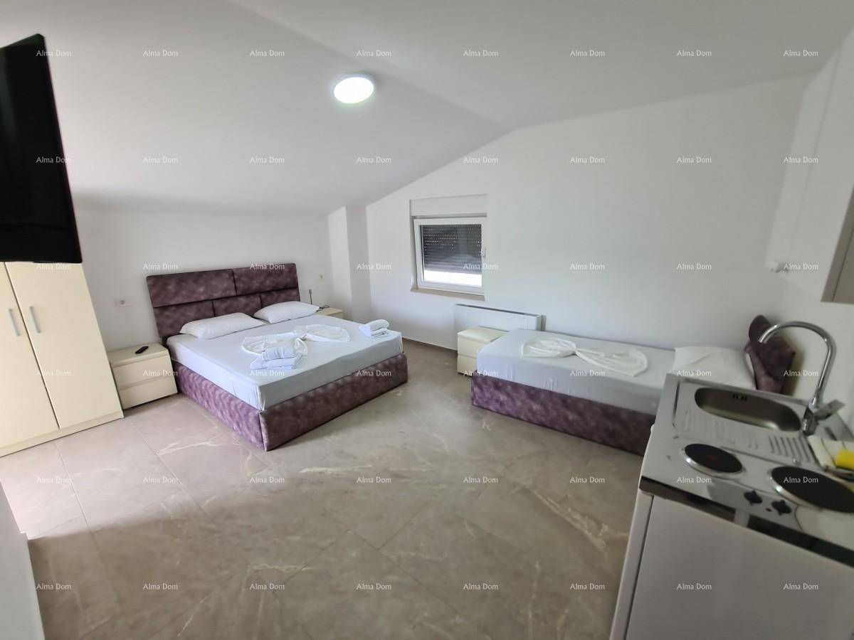 Geräumiges Studiozimmer mit Doppelbett, Einzelbett und einer kleinen Küchenzeile unter Dachschrägen.