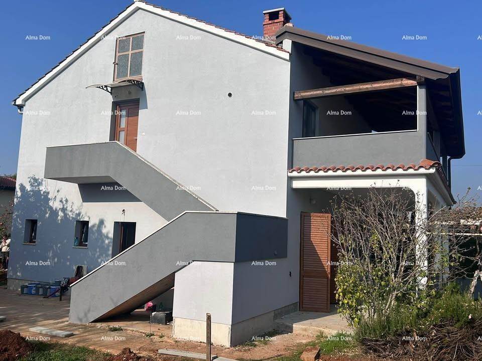 Modernes Haus mit grauer Fassade, Außentreppe und überdachter Terrasse.