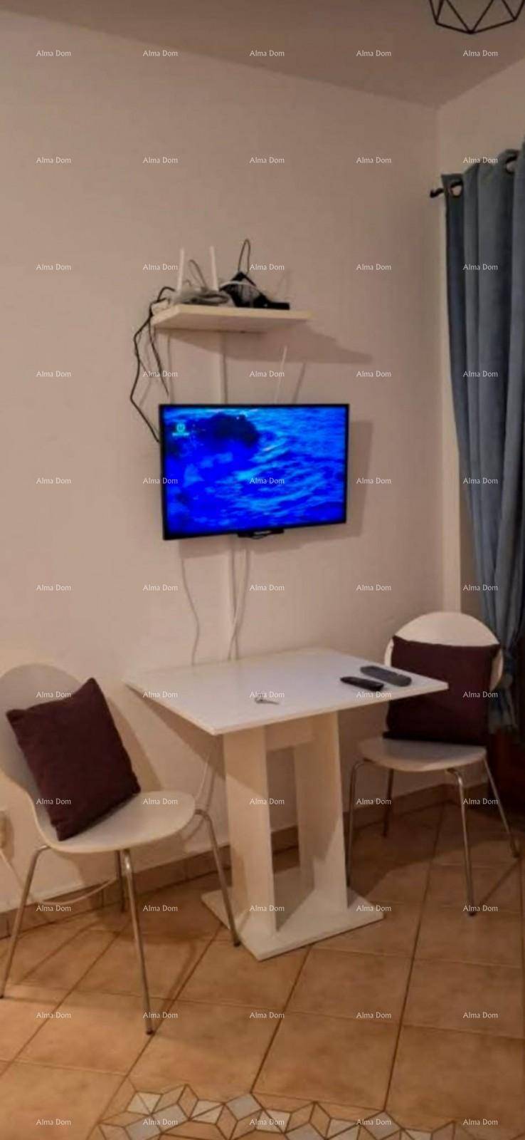 Kleiner Esstisch mit Stühlen, Wandfernseher und Fenster mit blauen Vorhängen in einem Wohnbereich.
