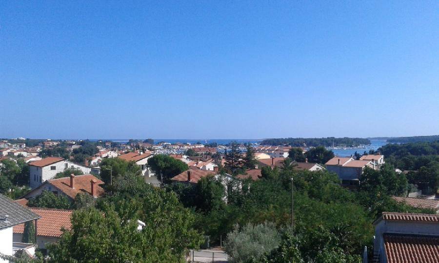 Panoramablick über eine Küstenstadt mit roten Dächern, üppigem Grün und dem weiten Meer im Hintergrund.