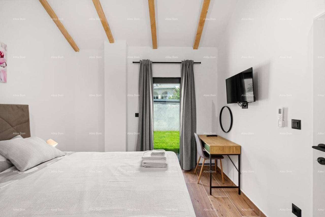Helles Schlafzimmer mit Holzbalken an der Decke, einem Schreibtisch und Blick ins Grüne.