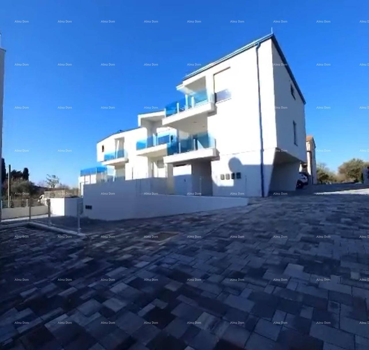 Seitenansicht des modernen Wohngebäudes mit blauen Balkonen und gepflasterter Zufahrt.