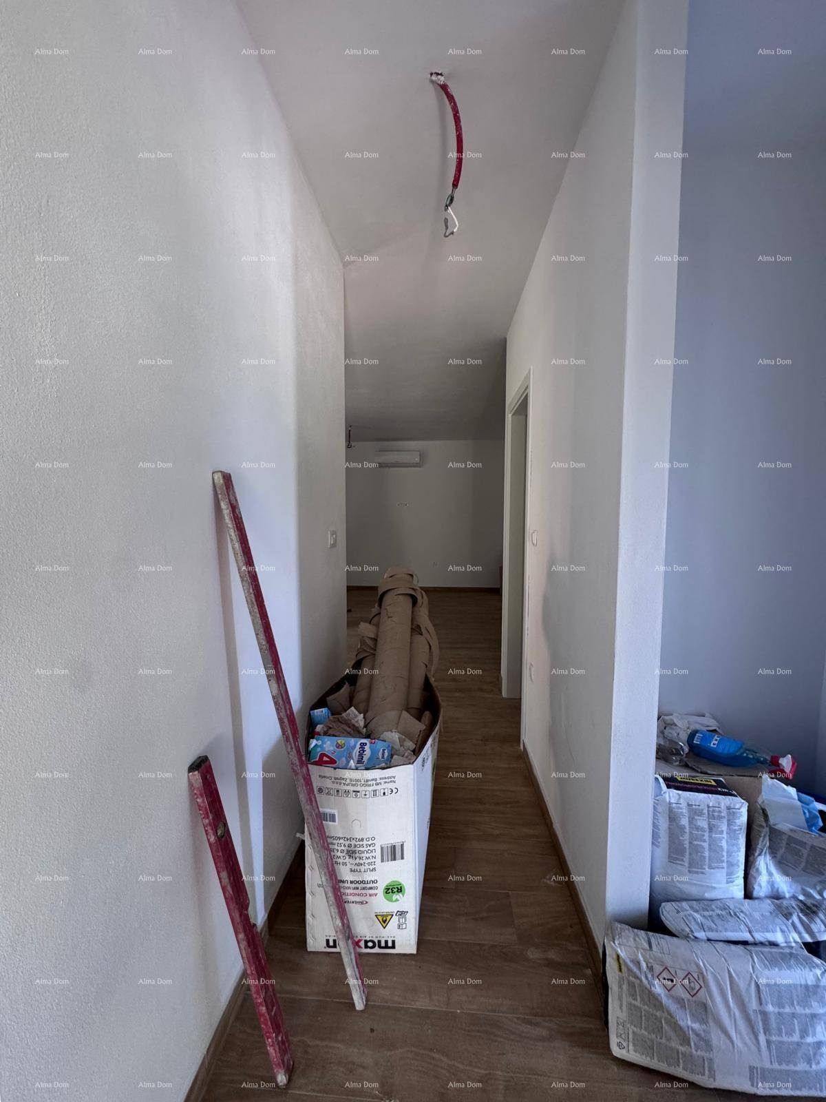Langer Flur mit Holzboden und weißen Wänden, derzeit mit Baumaterialien belegt.