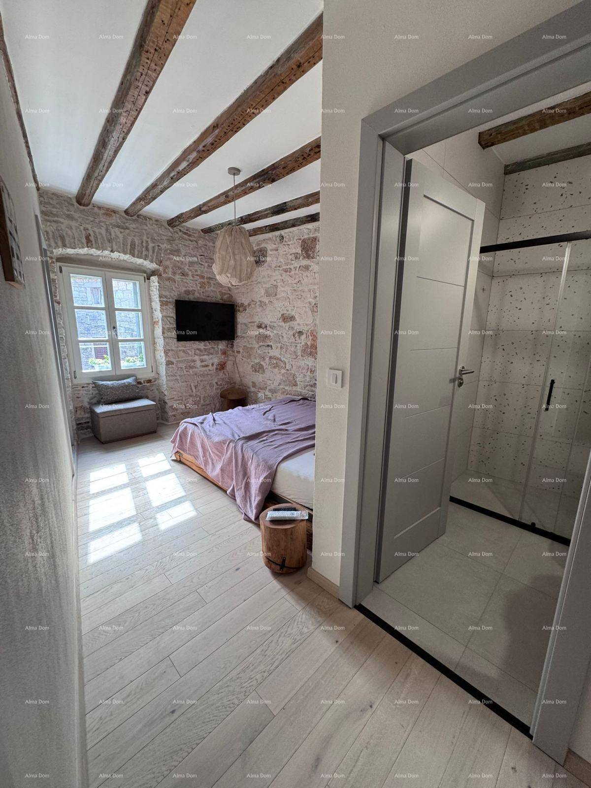 Schlafzimmer mit Holzbalkendecke, Steinwand und Zugang zu einem modernen Badezimmer.