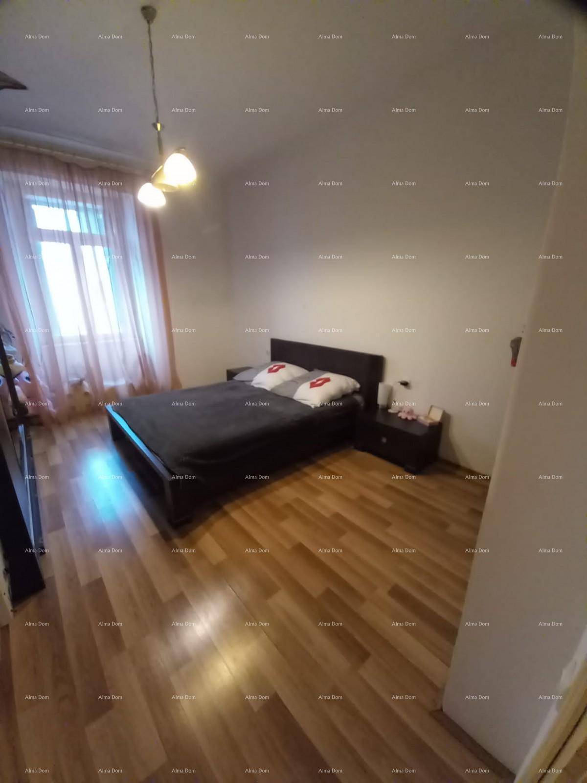 Schlafzimmer mit Doppelbett, Holzboden und Fenster mit hellen Vorhängen, schlicht eingerichtet.