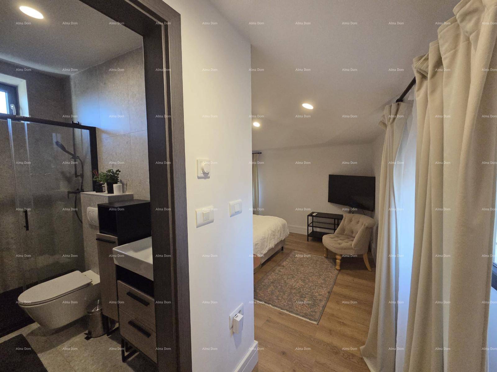 Blick vom Flur in ein Schlafzimmer mit TV und ein angrenzendes, modern gefliestes Badezimmer.
