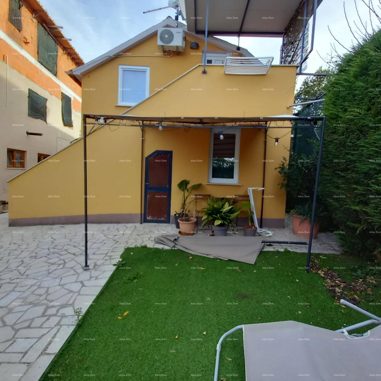 Gelb verputztes Gebäude mit Außentreppe und einem kleinen, begrünten Gartenbereich.