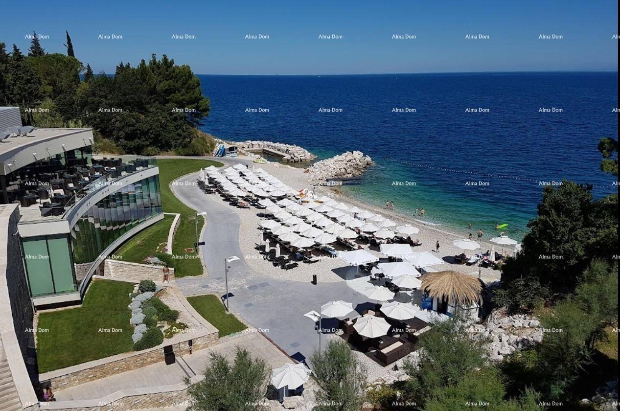 Panoramablick auf eine private Bucht mit Strand, Sonnenschirmen und einem modernen Gebäude.