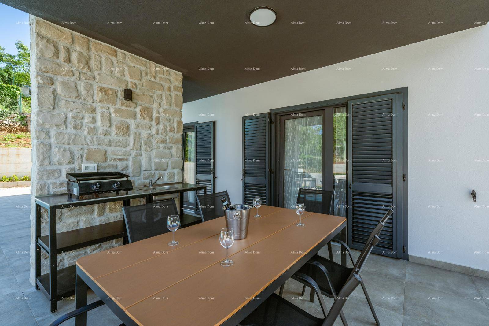 Überdachte Terrasse mit Esstisch, Steinsäule und Außenküche neben dem Poolbereich.