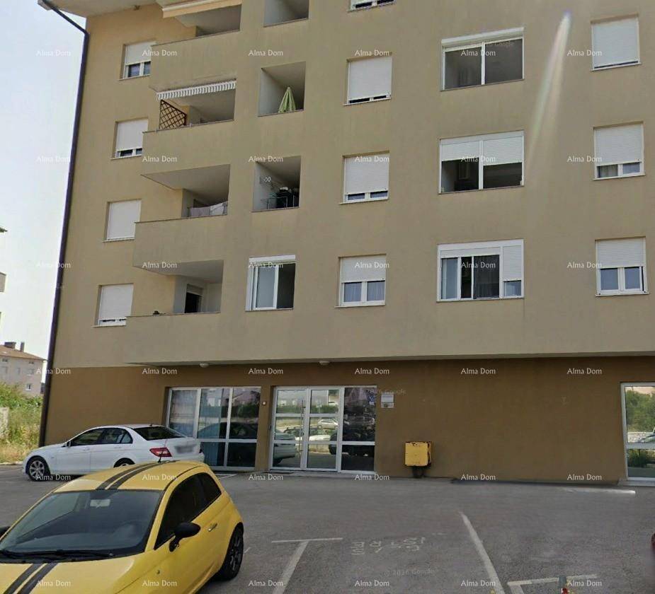 Mehrstöckiges Gebäude mit Balkonen und Fenstern, davor ein Parkplatz mit einem auffälligen gelben Auto.