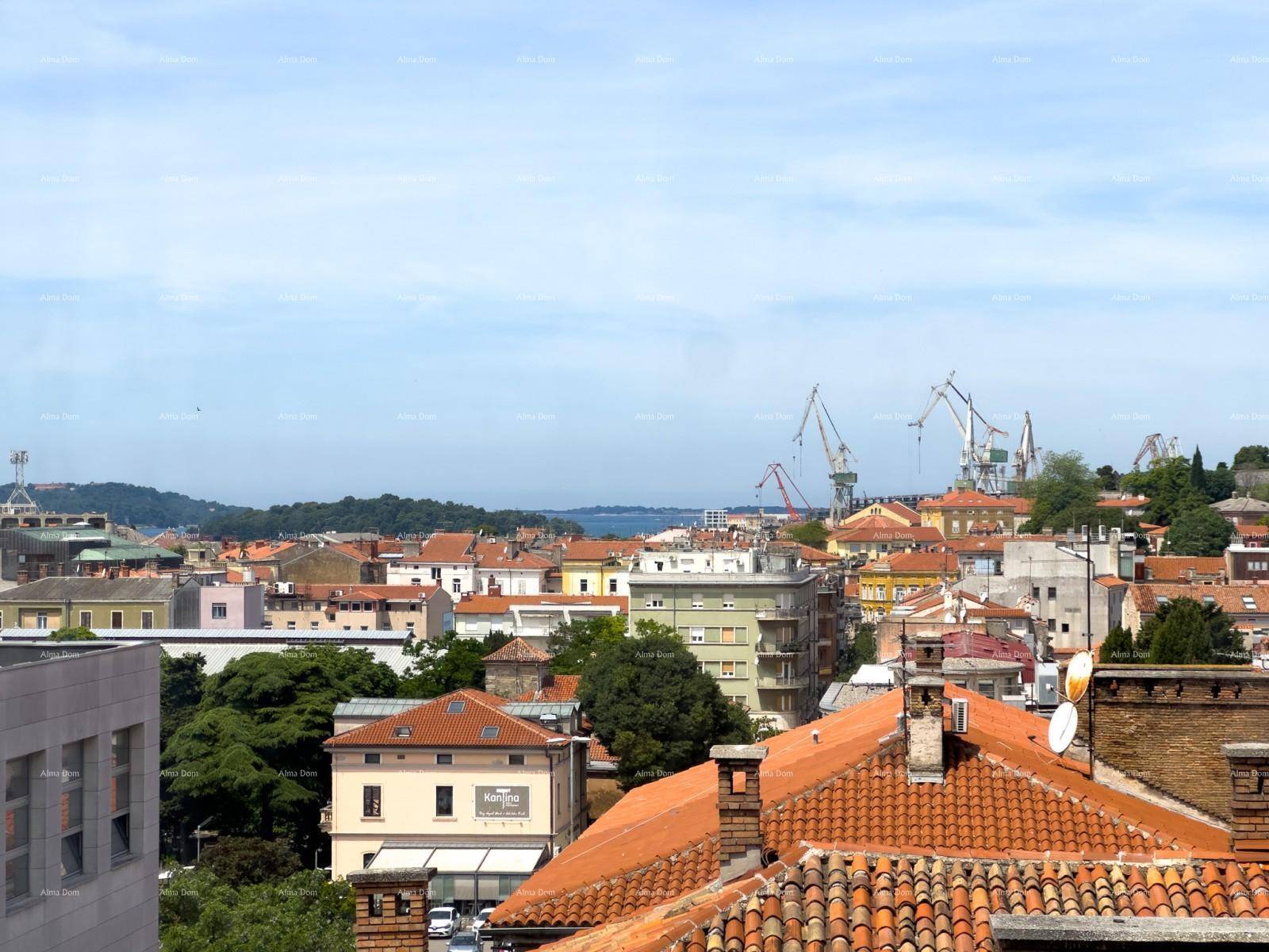 Panoramablick über die Stadt mit roten Dächern, Hafenkränen und dem Meer im Hintergrund.