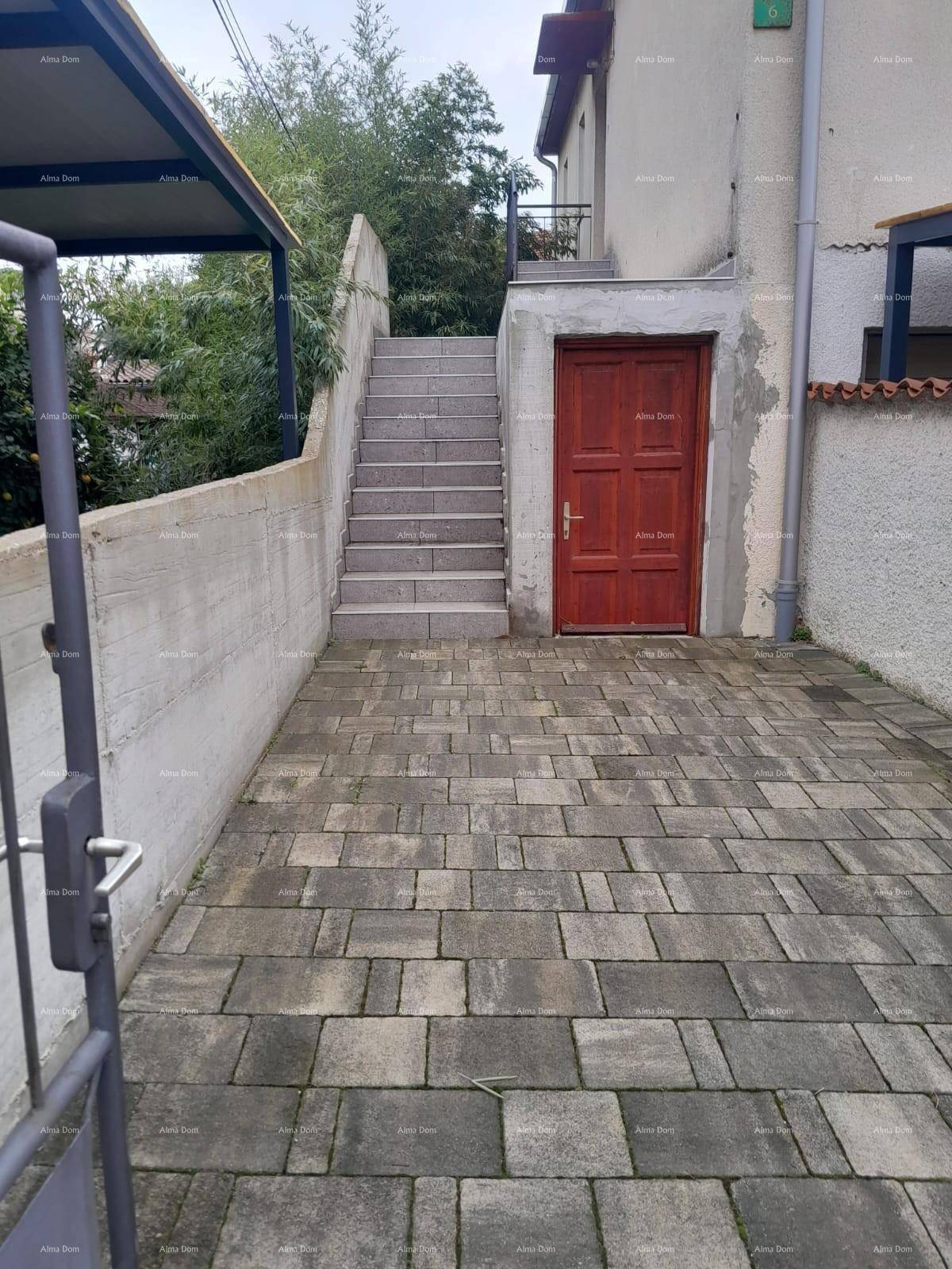 Gepflasterter Außenbereich mit Treppe und einer roten Tür, die zu einem Nebengebäude führt.