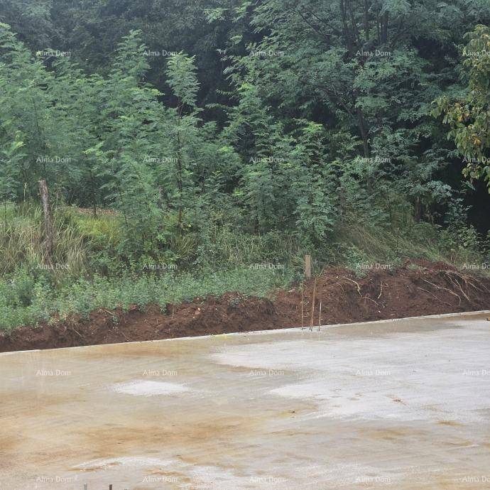 Teilansicht einer Betonfundamentplatte mit angrenzendem Erdhügel und dichtem Grün im Hintergrund.