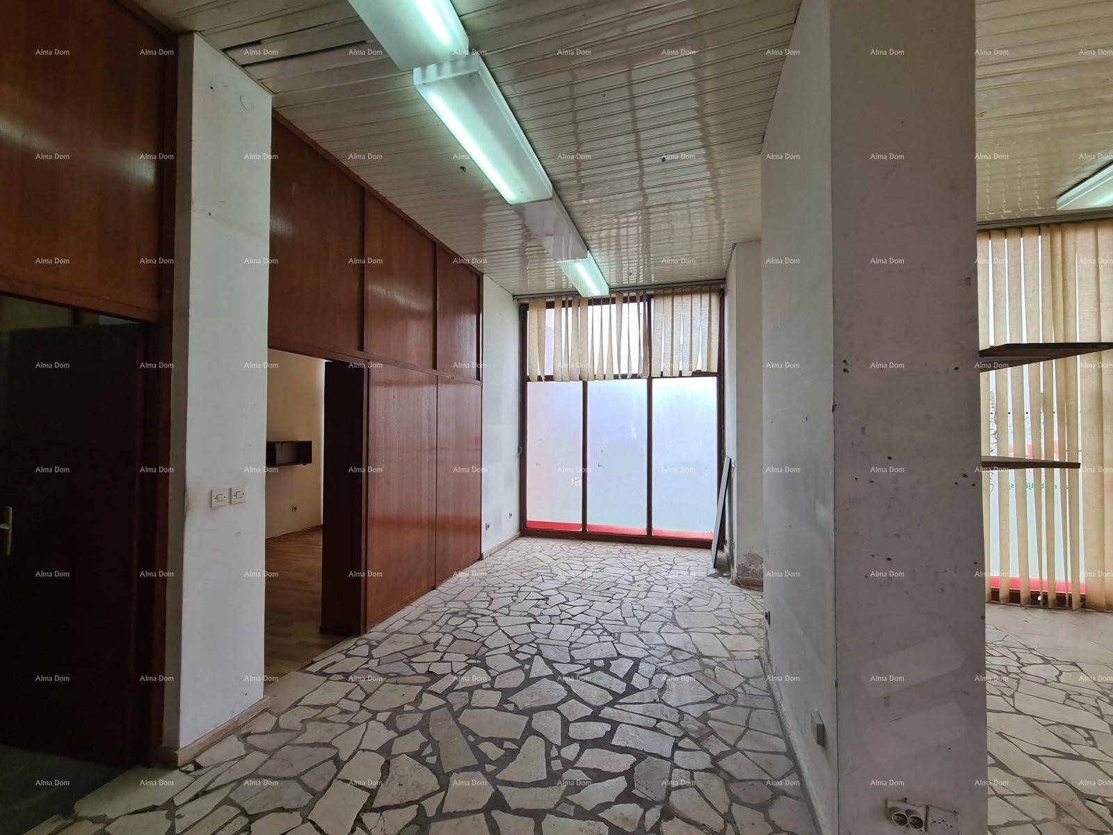 Langer Geschäftsraum mit Mosaikboden, Holzverkleidungen und großen Fenstern mit Jalousien.