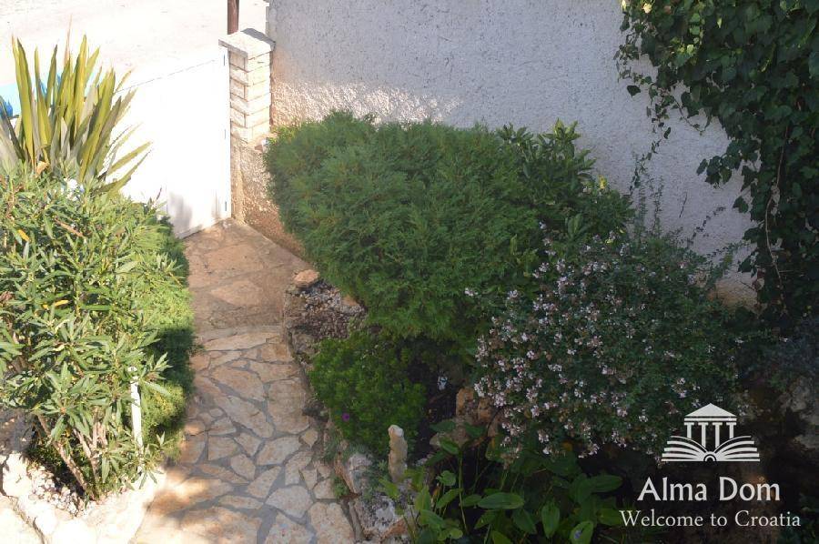Steinweg durch einen gepflegten Garten mit üppiger grüner Bepflanzung.