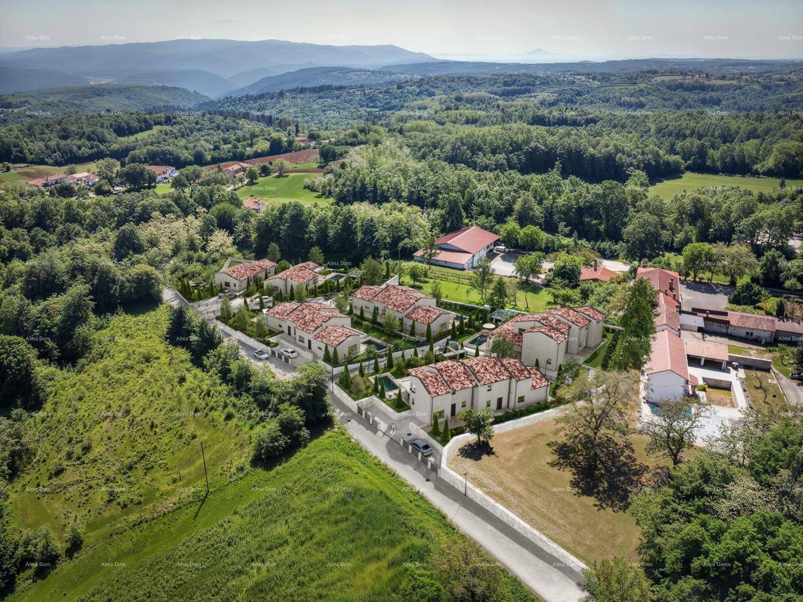 Weitläufige Luftaufnahme der modernen Villenanlage eingebettet in die hügelige, grüne Landschaft.
