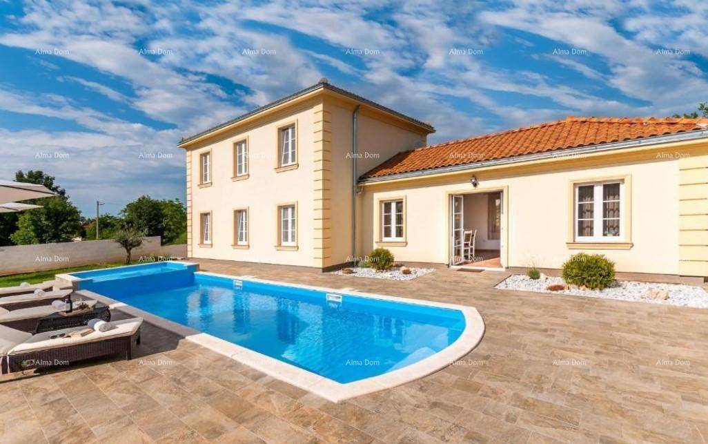 Ansicht der Villa mit großem Poolbereich, umgeben von einer gepflasterten Terrasse und Grünflächen.