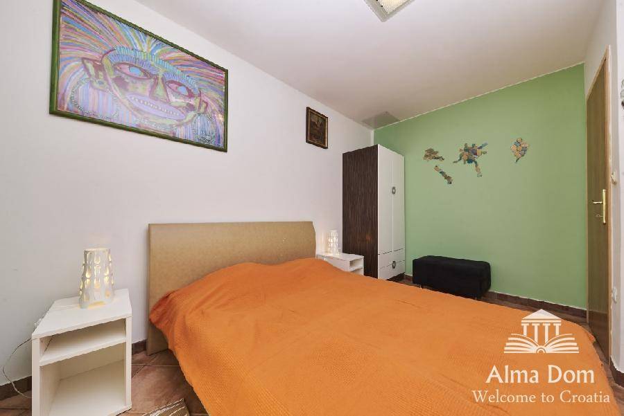 Helles Schlafzimmer mit orangefarbener Bettdecke, grüner Akzentwand und farbenfrohem Kunstwerk.