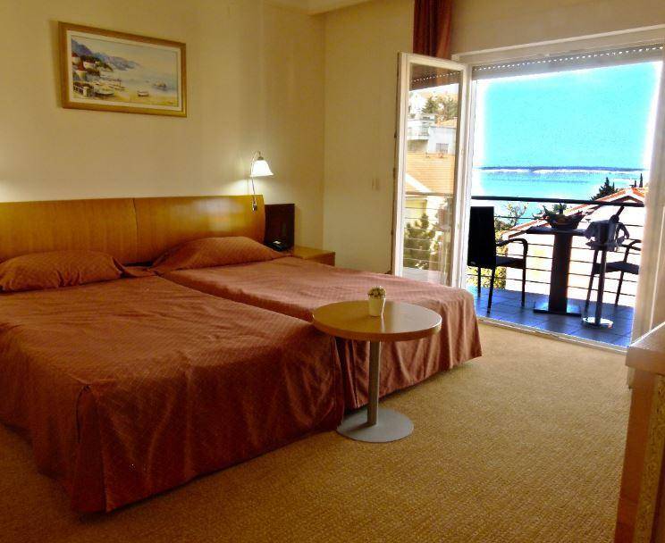 Gemütliches Schlafzimmer mit zwei Einzelbetten, Teppichboden und Zugang zu einem Balkon mit Meerblick.