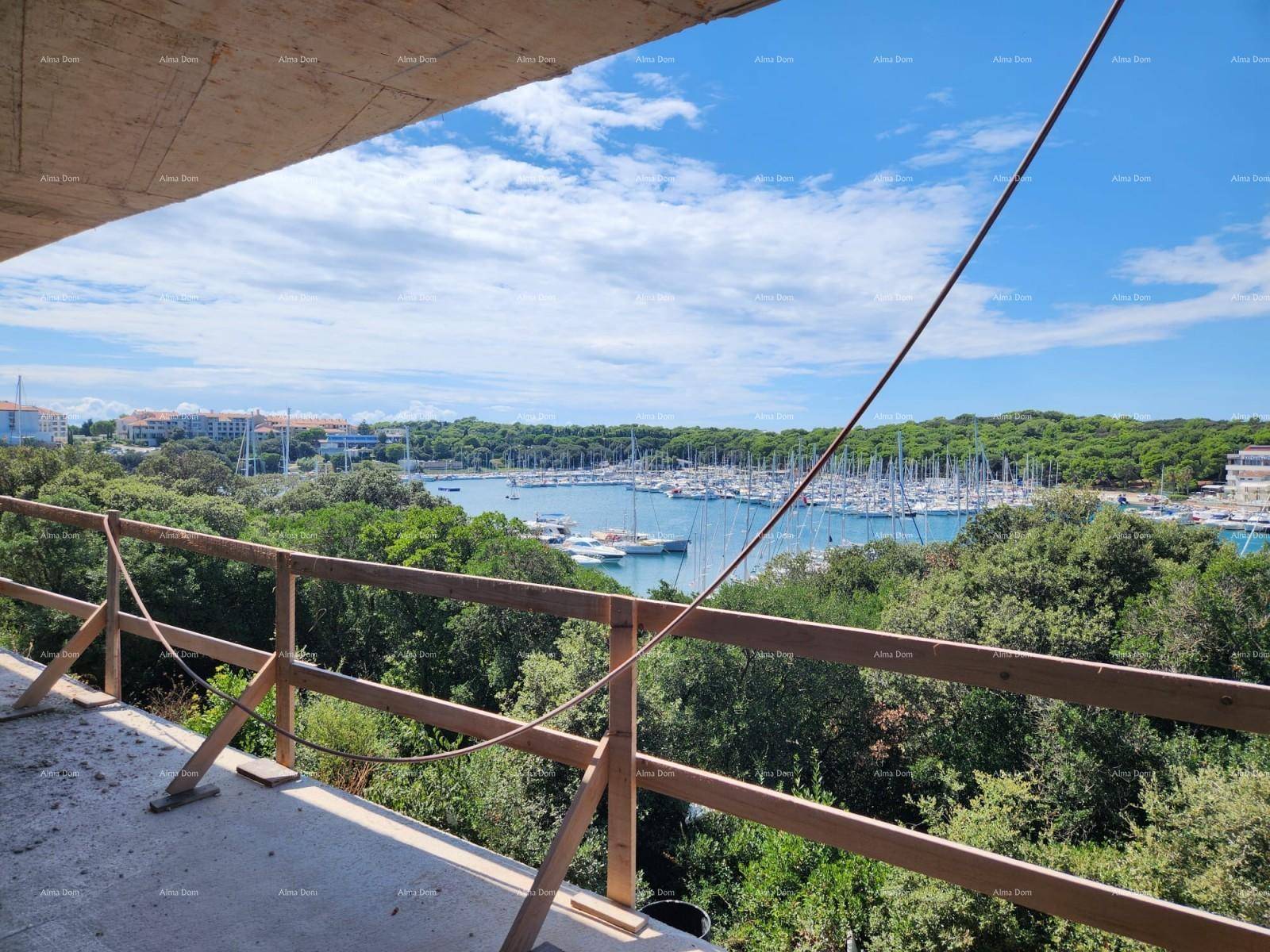 Blick von einem unfertigen Balkon auf den Yachthafen und die bewaldete Küste unter blauem Himmel.