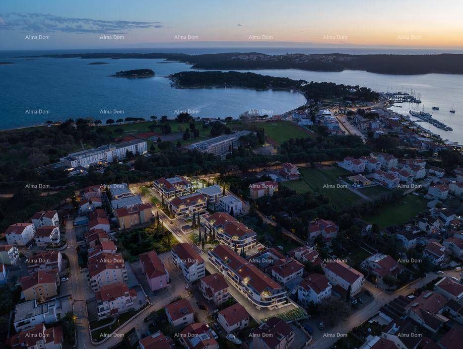 Abendliche Luftaufnahme des Wohnkomplexes mit beleuchteten Gebäuden und Blick auf die Bucht und Stadt.