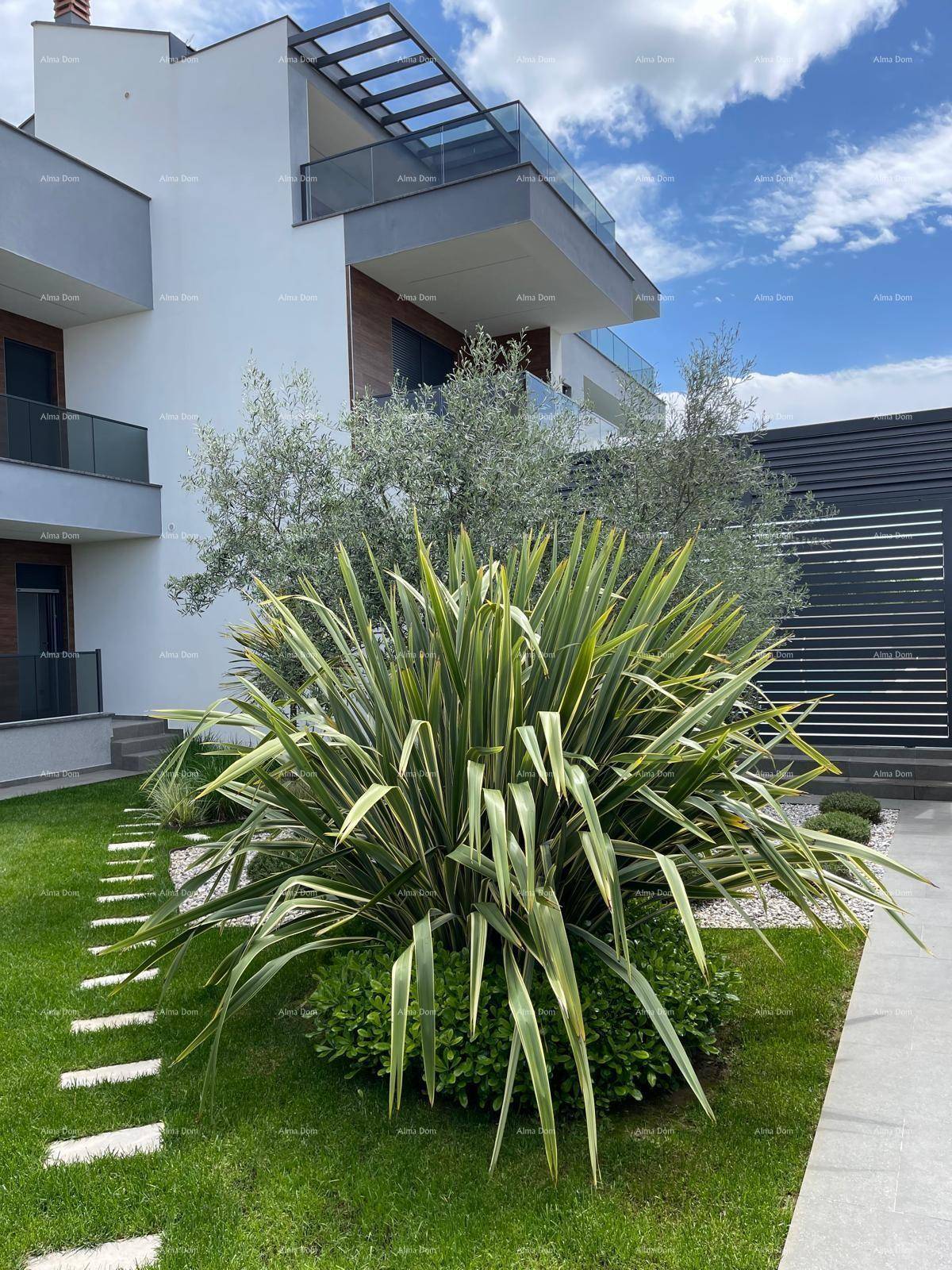 Moderne Architektur der Villa mit gepflegtem Vorgarten und mediterranen Pflanzen unter blauem Himmel.