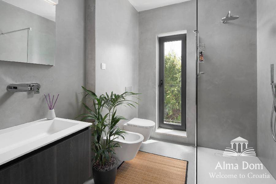 Elegantes Badezimmer in Grau mit begehbarer Dusche, Bidet und hohem Fenster für Tageslicht.