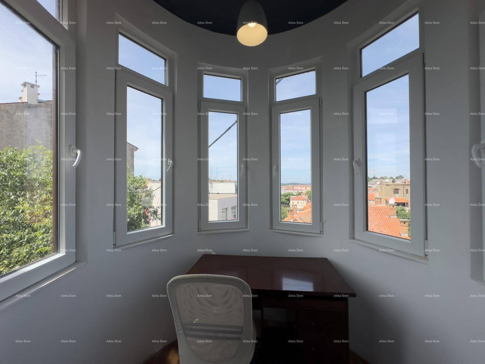 Heller Arbeitsbereich mit vielen Fenstern, einem Schreibtisch und Blick auf die Stadt.