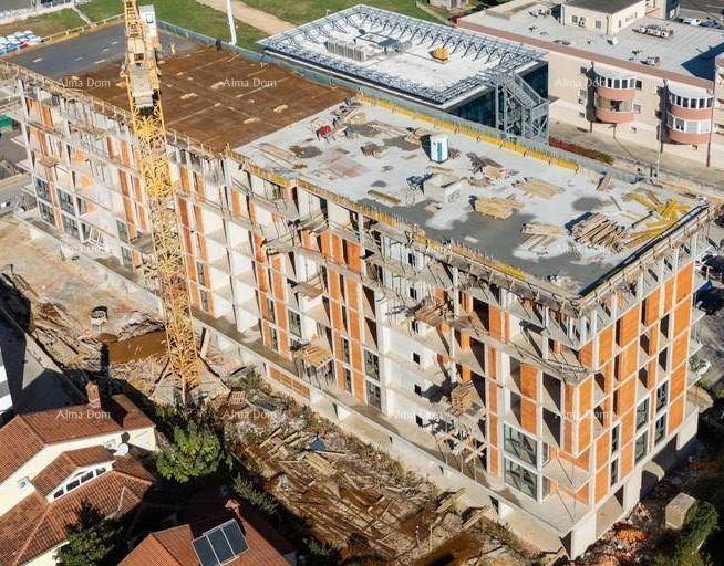 Eine Luftaufnahme zeigt das im Bau befindliche Apartmentgebäude mit sichtbarer Beton- und Ziegelkonstruktion.