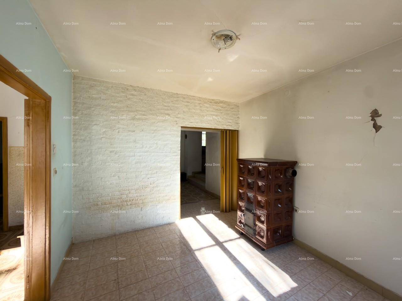 Wohnraum mit Kachelofen, Fliesenboden und einer Wand mit Ziegelverkleidung, durchflutet von Sonnenlicht.