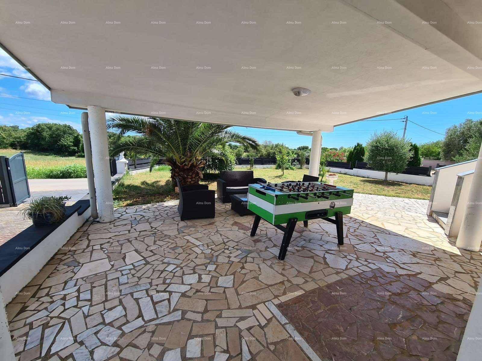 Überdachte Terrasse mit einem Kickertisch und Loungemöbeln, umgeben von einem Gartenbereich.