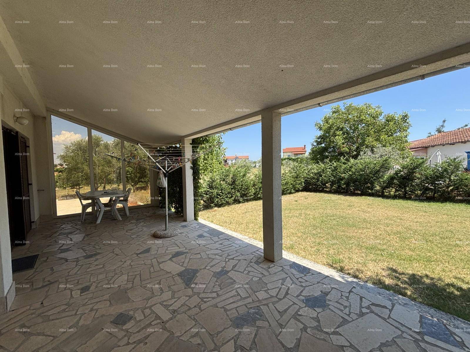 Überdachte Terrasse mit Steinfliesen, Gartenmöbeln und Blick auf den Rasen.