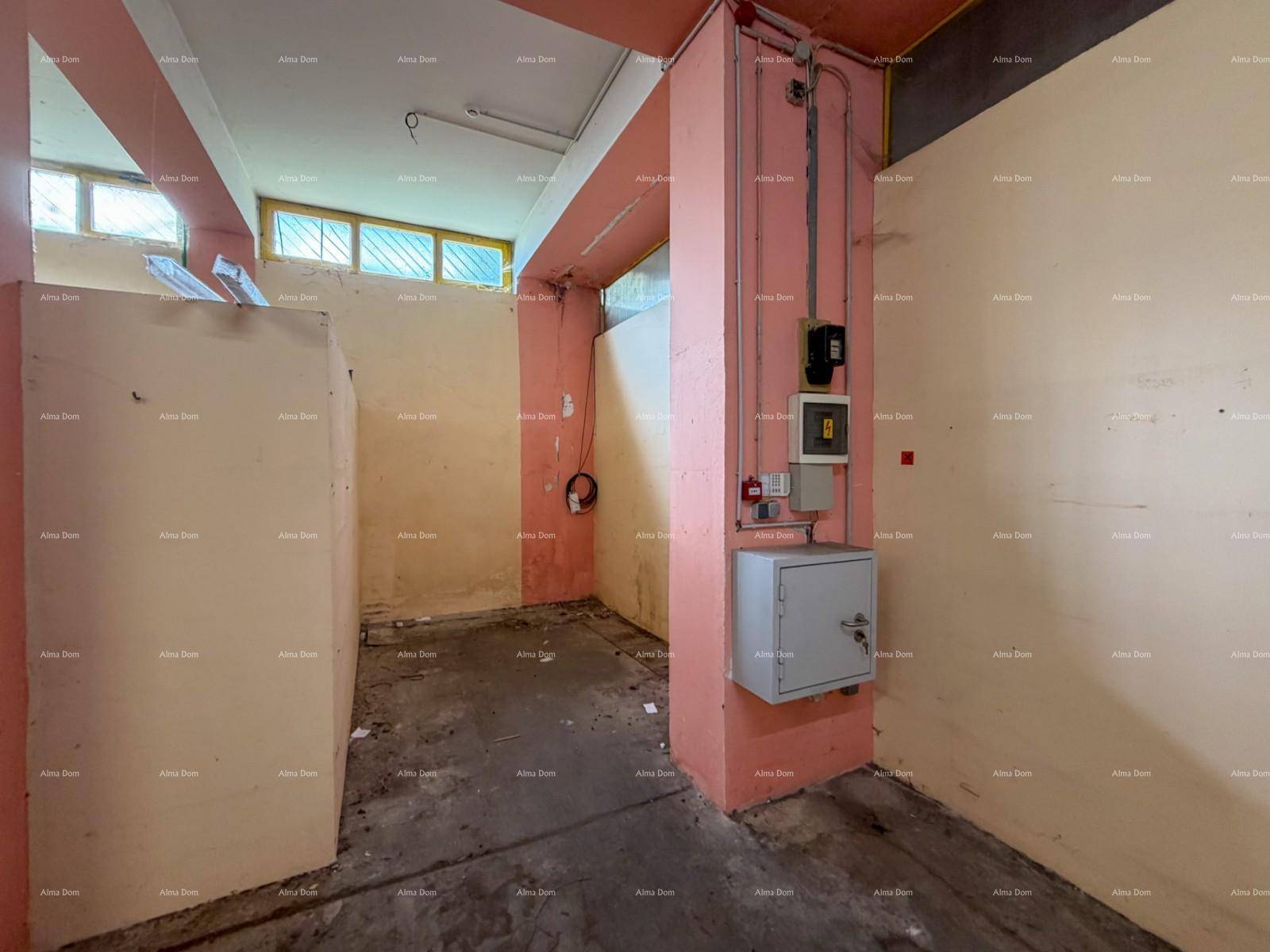Ecke des Lagerraums mit elektrischen Installationen, einem Safe an einem rosa Pfeiler und kleinen Fenstern.