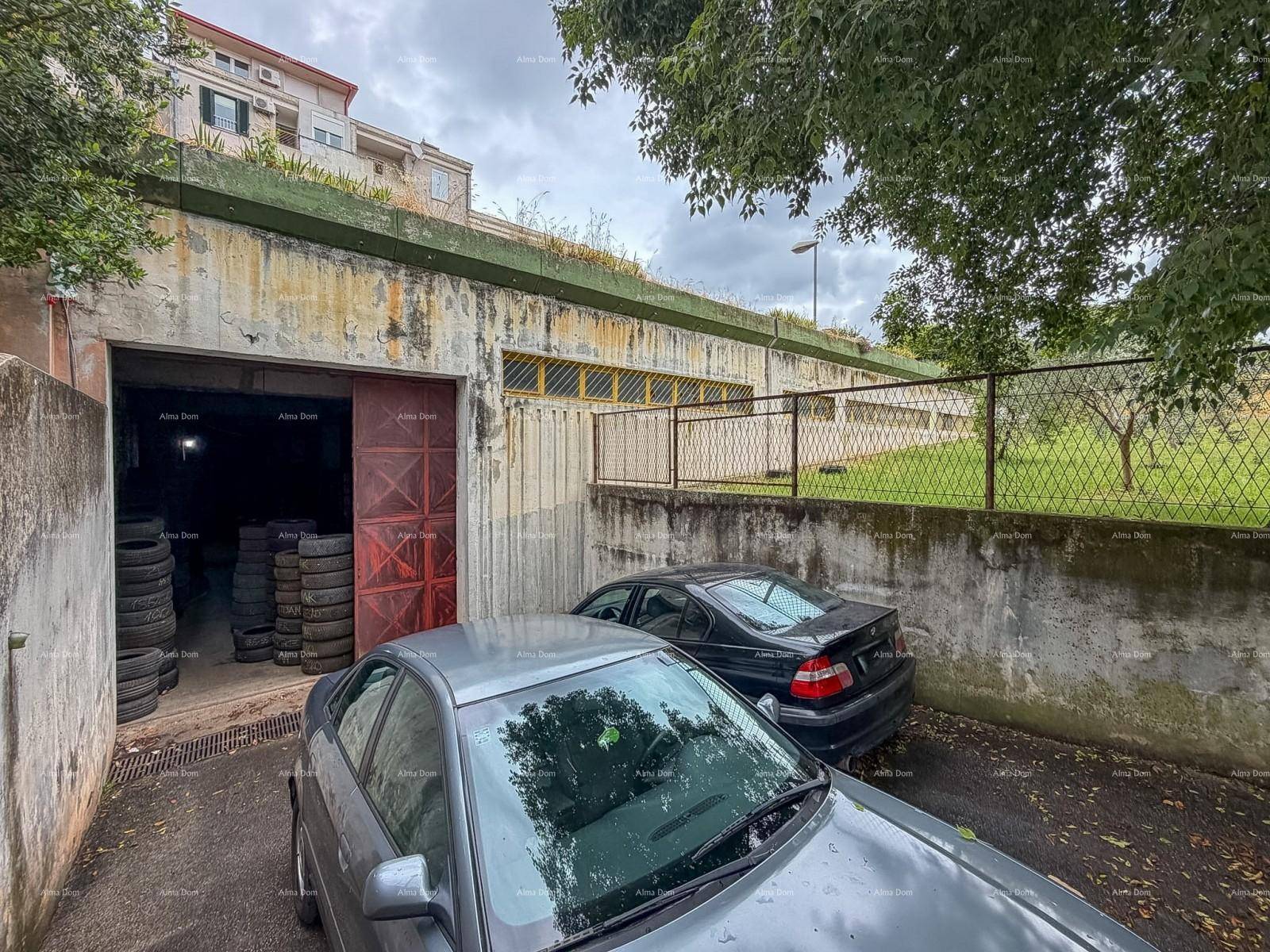 Außenansicht einer Garageneinfahrt mit gestapelten Reifen, zwei Autos davor und einer Betonmauer mit Zaun.