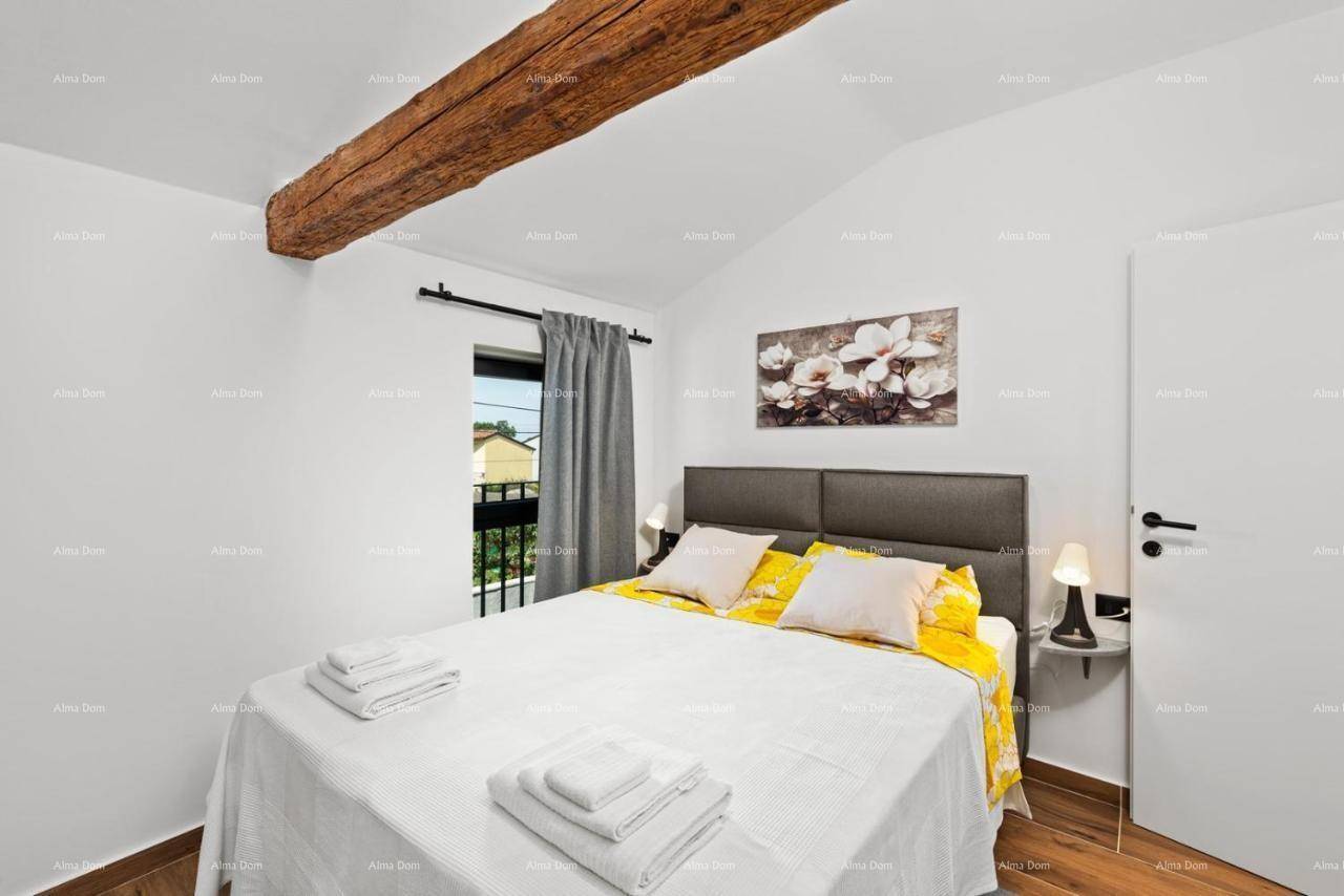 Helles Schlafzimmer mit Doppelbett, Holzbalken und Zugang zu einem kleinen französischen Balkon.