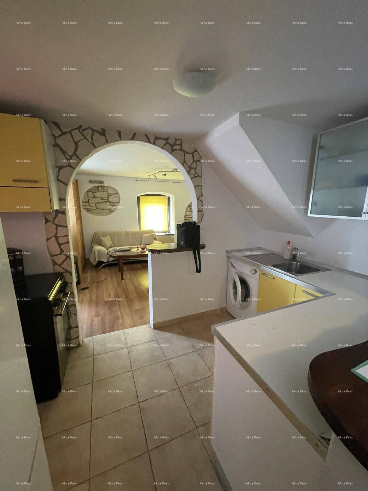 Kleine Küche mit Waschmaschine, Spüle und Blick durch einen Steinbogen in den Wohnbereich.