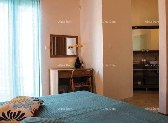 Helles Schlafzimmer mit Bett, Schminktisch und Zugang zu einer kleinen Kochnische.