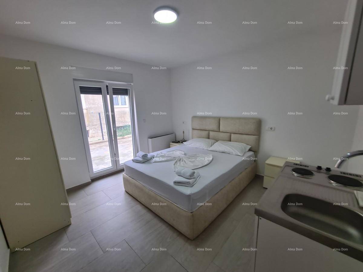 Schlafzimmer mit Doppelbett, Nachttisch und integrierter Küchenzeile, mit Zugang nach draußen.
