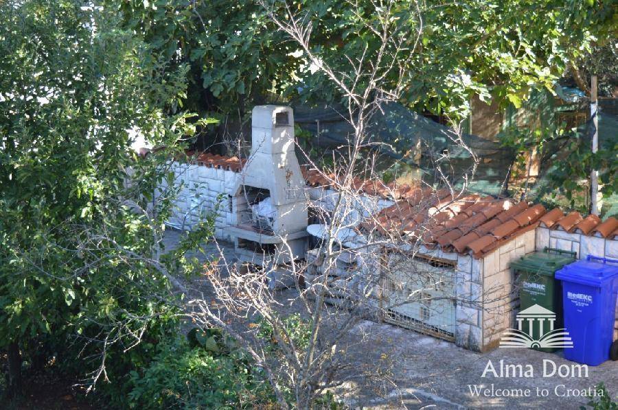 Gartenbereich mit einem gemauerten Grill und viel Grün, umgeben von Bäumen.