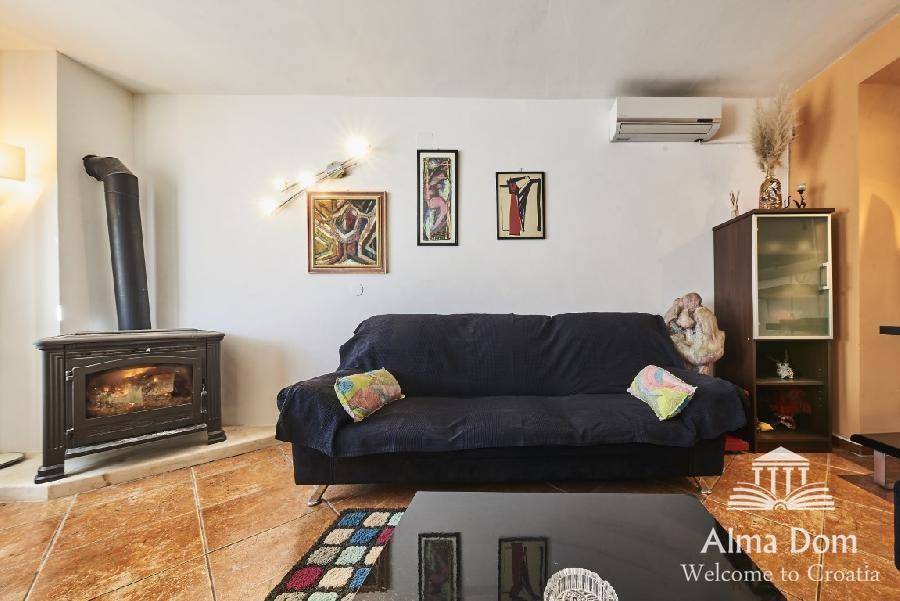 Gemütliches Wohnzimmer mit Kaminofen, Sofa und farbenfrohen Kunstwerken an der Wand.
