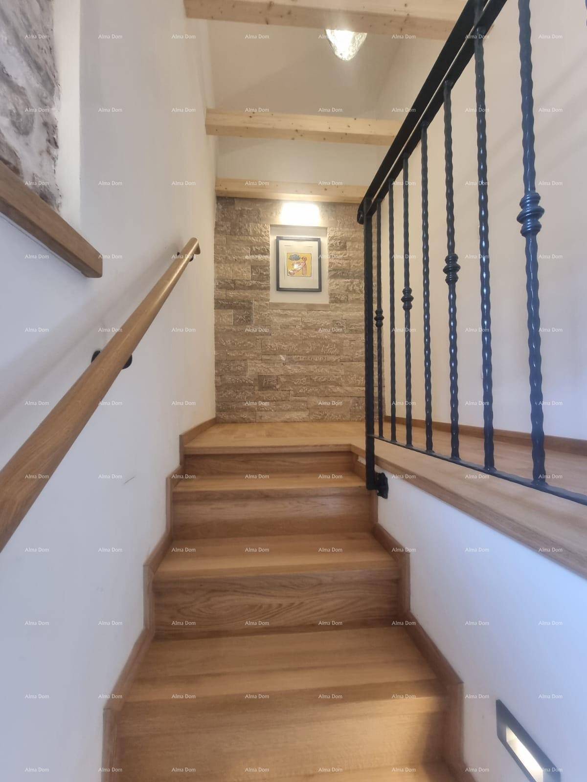 Holztreppe mit schmiedeeisernem Geländer und Steinwand im Treppenhaus.