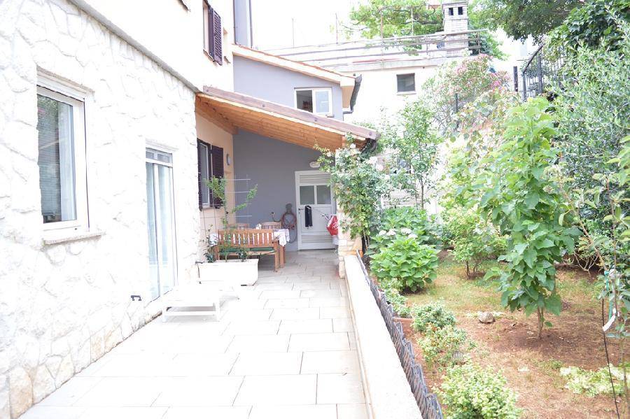 Lange gepflasterte Terrasse mit Holzdach und angrenzendem grünen Gartenbereich.