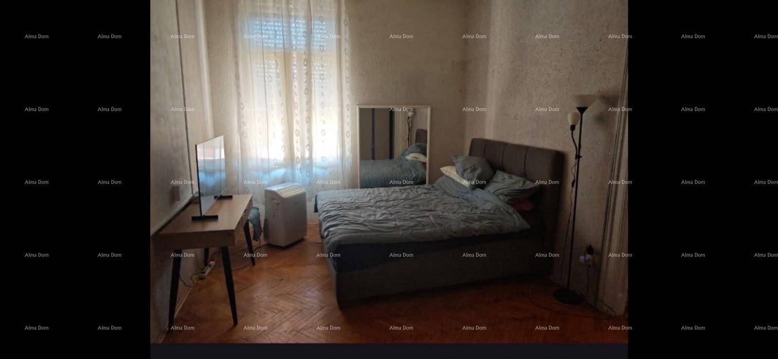 Schlafzimmer mit Bett, Schreibtisch und Fernseher, hell durch ein großes Fenster.
