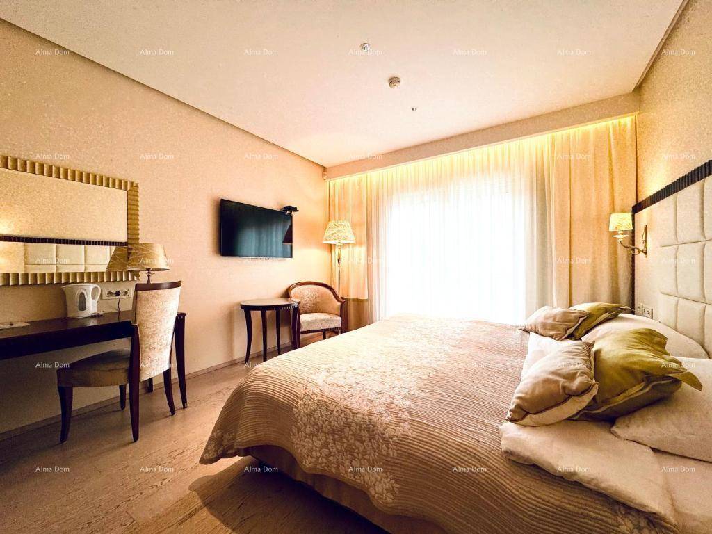 Helles Schlafzimmer mit großem Doppelbett, Schreibtisch und Fernseher, beleuchtet durch ein großes Fenster.