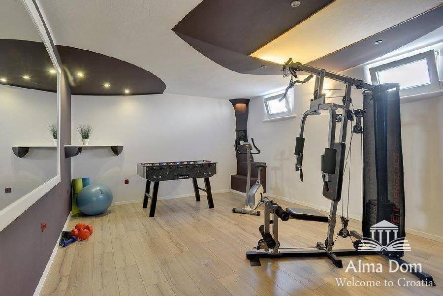 Fitnessraum im Keller mit Trainingsgeräten, Tischfußball und indirekter Beleuchtung.