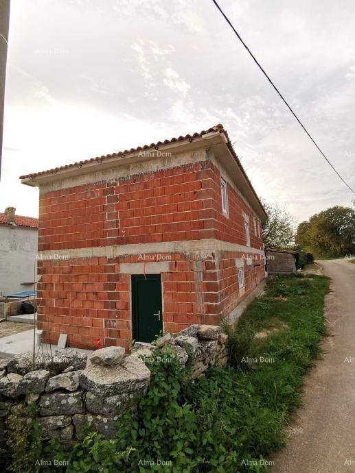 Rohbau eines Hauses mit roten Ziegelwänden, grüner Tür und einer Steinmauer im Vordergrund.