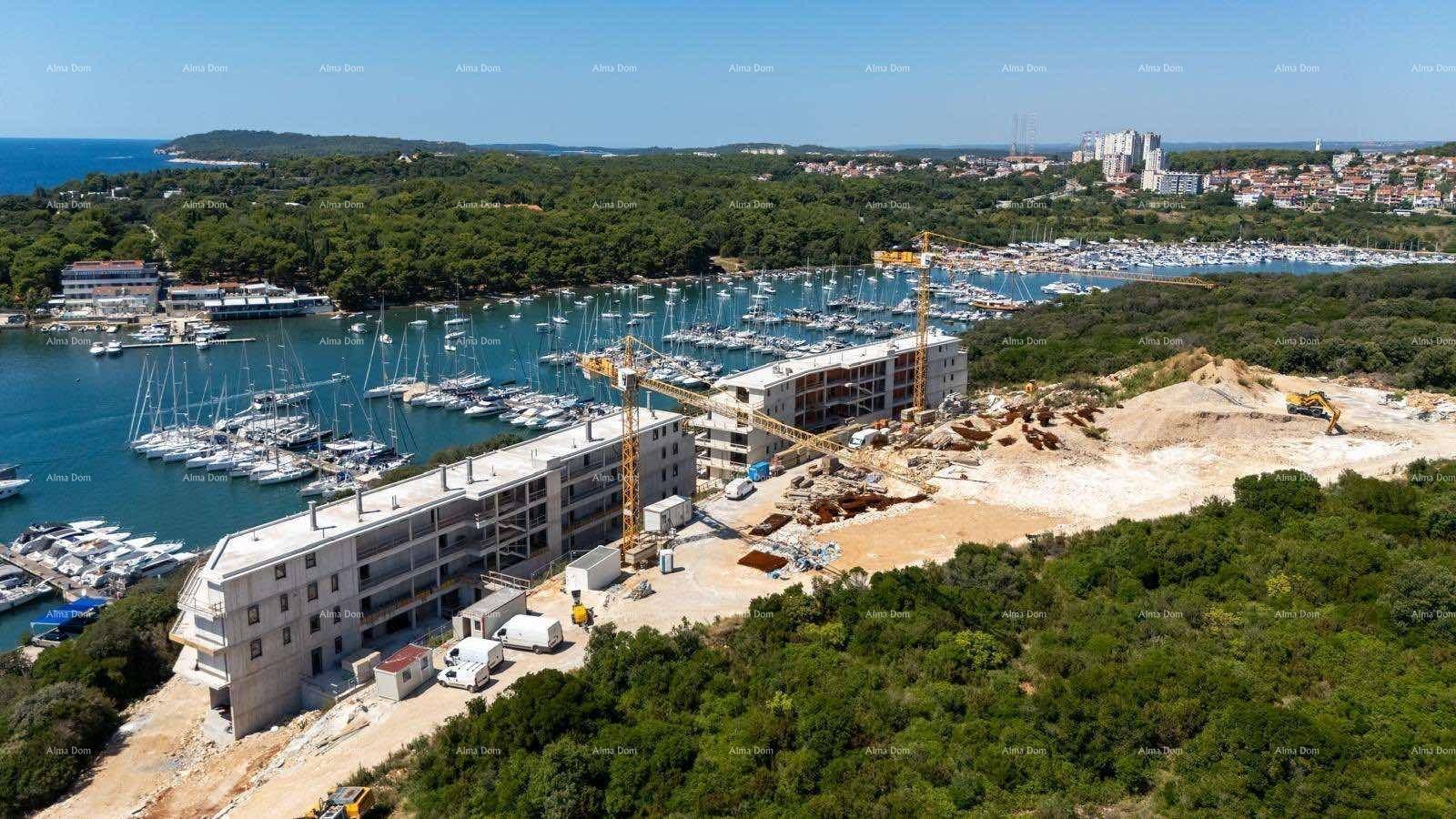 Luftaufnahme einer Baustelle mit zwei im Bau befindlichen Gebäuden und einem Yachthafen im Hintergrund.